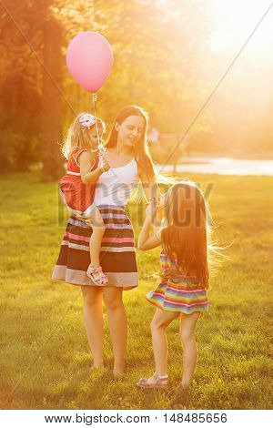 Mother and two daughters for a walk in the park. Mother holds daughter on hands. Family time together. Cheerful picnic.