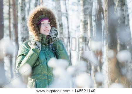 Young attractive woman is holding woolly mittens near her head in winter forest outdoors