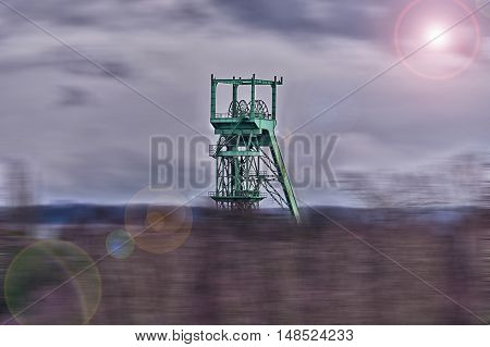 Image with lens flare effect and blur: Age headframe industrial monument in the Ruhr area before dawn sky with clouds.