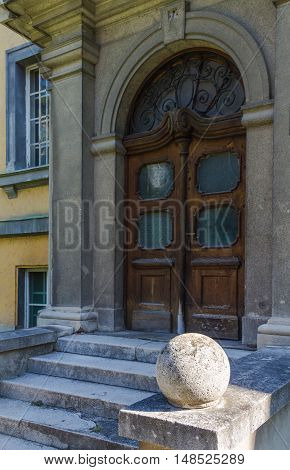 Side view on the entrance to an old building. Heavy wooden door with an arch. Stairs in a shadow and a stone ball enlightened by the sunlight.