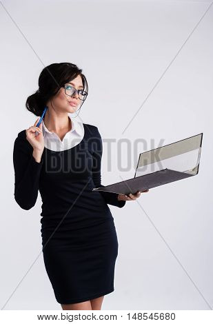 Young Caucasian woman wearing a dark blue dresst and and a white shirt, holding a ring binder folder and pen. Isolated on light background