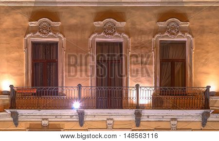 Three windows in a row and balcony on night illuminated facade of urban office building front view St. Petersburg Russia