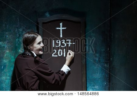 Halloween theme: Portrait of a young smiling girl in school uniform as killer woman against school board . The image in the style of Halloween and Addams family