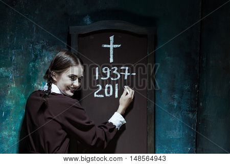 Halloween theme: Portrait of a young smiling girl in school uniform as killer woman against school board . The image in the style of Halloween and Addams family