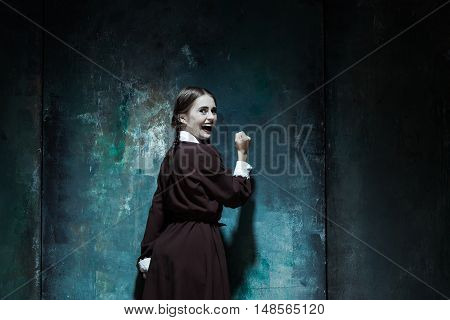 Halloween theme: Portrait of a young smiling girl in school uniform as killer woman against school board . The image in the style of Halloween and Addams family