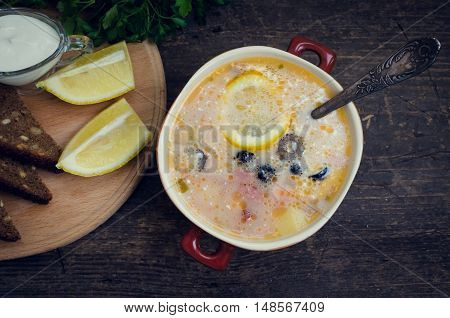 Solyanka - Russian traditional meat soup with hot spices in a bowl with bread and spoons on old wooden background. Meat solyanka - traditional Russian dish. Russian cuisine concept. Top view.