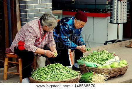 Luo Dai China - October 13 2007: Two Chinese women seated on bamboo stools on a sidewalk selling green beans and scallions displayed in baskets