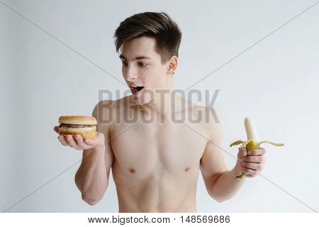 Young man choosing a food. Dieting guy with a burger and banana