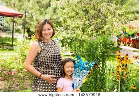 Happy pregnant asian mom and child girl hugging. The concept of childhood and family. Beautiful Mother and her baby outdoor