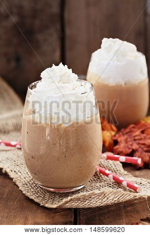 Pumpkin Smoothies with whipped cream against a rustic background. Shallow depth of field with selective focus on dessert in foreground.