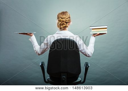 Ebook vs book. Woman sitting on chair holding traditional book and e-book reader tablet touchpad pc back view grunge background.