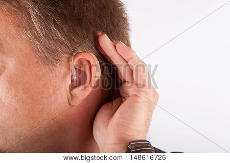 Close up ear of a man wearing hearing aid cupping his hand behind his ear