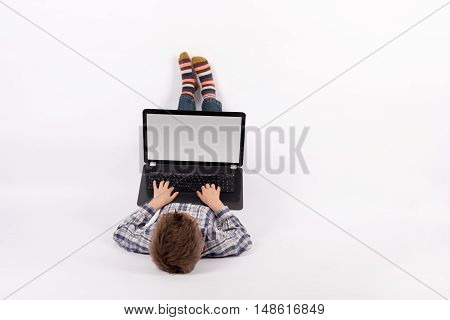 Young boy lying and using a laptop with empty screen suitable for text. Studio shot with white background.
