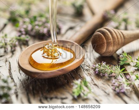 Herbal honey pouring into the wooden spoon. Spoon is on old wooden table surrounded with levender flowers.