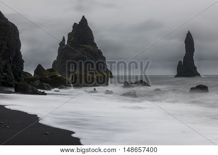 Reynishverfisvegur Reynisfjara black sand beach with rocks ocean and dark rain and storm clouds near the village of Vik in Iceland.