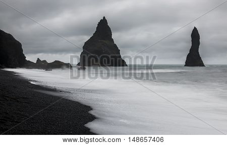 Reynishverfisvegur Reynisfjara black sand beach with rocks ocean and dark rain and storm clouds near the village of Vik in Iceland.