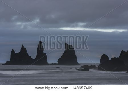 Reynishverfisvegur Reynisfjara black sand beach with rocks ocean and dark rain and storm clouds near the village of Vik in Iceland.