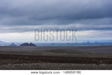Volcanic landscape on Iceland with mountains lava and black sand and dark rain clouds in the sky.