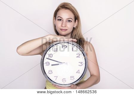 Beautiful young woman looking at a large silver retro clock that she is holding, she wonders how much time passed