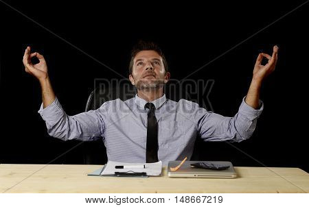 young attractive happy businessman relaxing with hands in yoga position cheerful and friendly wearing shirt and tie isolated in black background sitting at office desk chair in relax at work concept