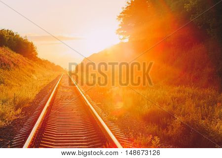 The Scenic Landscape With Railway Going Straight Ahead Through Summer Hilly Meadow To Sunset Or Sunrise In Sunlight. Lense Flare Effect.