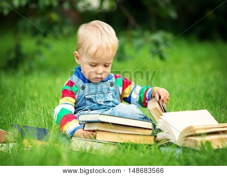 one year old baby reading a book sitting on the grass in garden