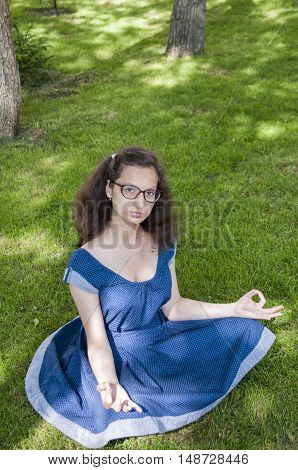 Girl in blue dress meditates on the grass