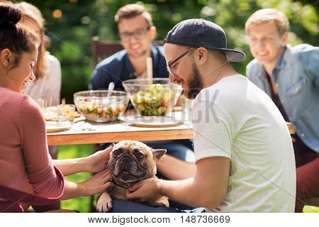leisure, holidays, eating, people and food concept - happy friends with french bulldog dog having dinner at summer garden party