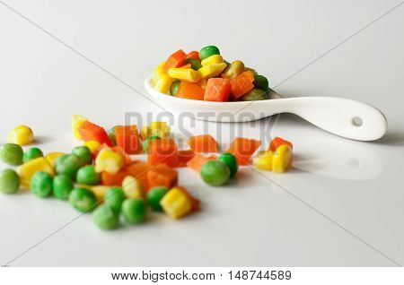 Vegetables three colors carrots kernels peas in spoon white background