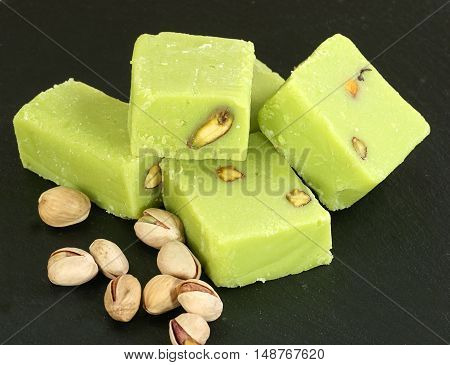 five pieces of pistachio barfi with nuts on a dark slate