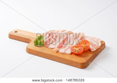 Thin slices of fresh streaky bacon on cutting board