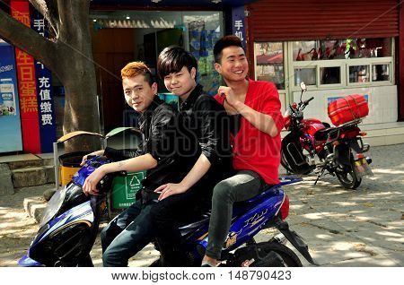 Pixian China: March 27 2013: Three Chinese youths riding a motorcycle along the town's main street