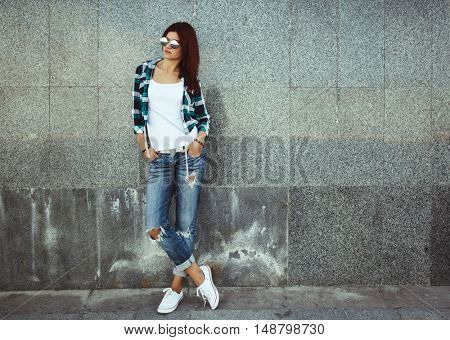Hipster girl wearing white t-shirt, fashion sunglasses and jeans posing against wall, swag street style