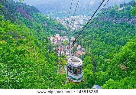 BORJOMI GEORGIA - MAY 27 2016: The small cable car among the green mountains of Borjomi-Kharagauli Nature Reserve with the spa resort in gorge on May 27 in Borjomi.