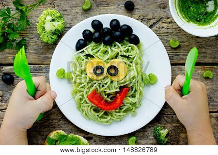Food art idea for kids green monster from spaghetti olives and bell pepper. Child eating concept top view