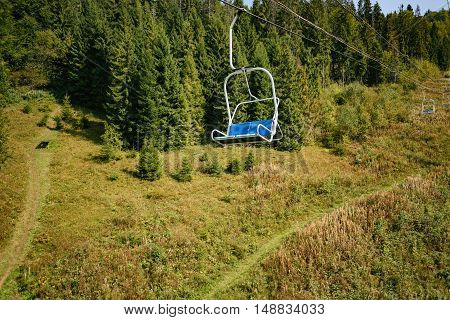 Lift seats in the Carpathians among spruce trees with walkway. Summer time