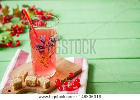 Fresh viburnum drink in glass on green wooden background with leaves and berries. Selective focus.