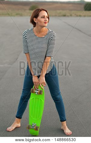 Girl with skateboard standing barefoot on the asphalt.