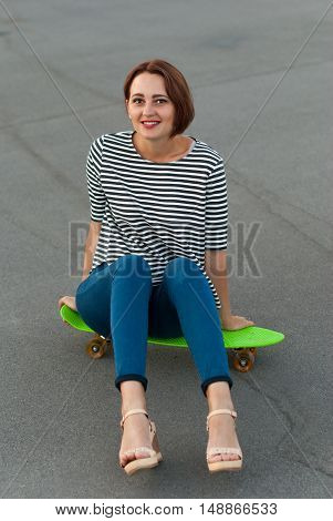 Attractive girl sitting on a skateboard in the street.