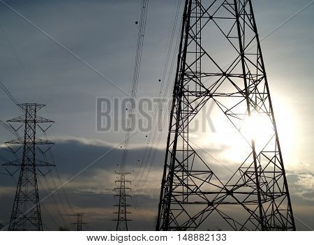 silhouette of steel framework of high voltage pylon tower with electric transmission power lines and aircraft warning ball and evening sunset sky, infrastructure domestic electric energy industry