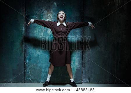 Halloween theme: Portrait of a young smiling girl in school uniform as killer woman against school board . The image in the style of Halloween and Addams family