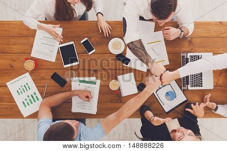 Team bump fists, show connection and alliance, top view of working table. Teambuilding in office, young businessmen and women in casual unite hands for teamwork and cooperation at new project.