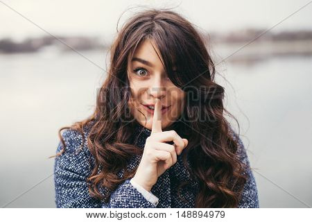 cute woman with long black hair holding her finger on her mouth as she was keeping a secret