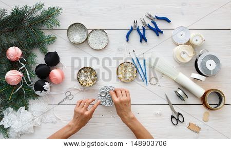 Making handmade christmas balls. Woman's leisure, tools for creating holiday decorations and garland. Top view of white wooden table with female hands holding various trinkets, decor accessories