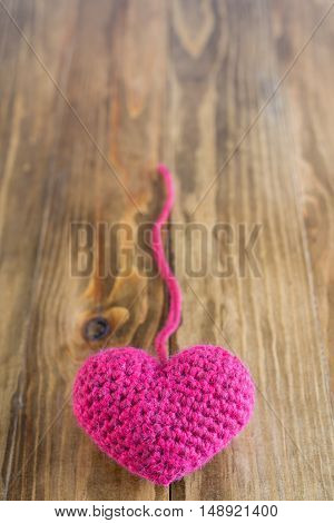 A chrocheted heart with a thread on a wooden background. Soft focus on a heart.