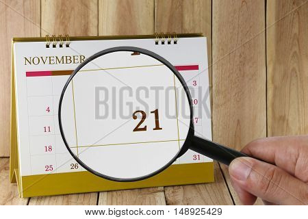 Magnifying glass in hand on calendar you can look Twentieth one day of month. Focus number twenty-one in November. Concept in business and meetings.