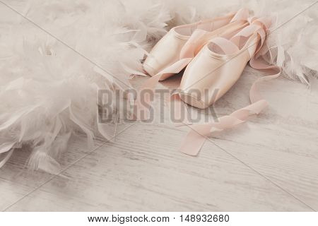 Pastel pink ballet shoes background. New pointe shoes with satin ribbon lay on white rustic shubby chic wood near feather boa, view with copy space