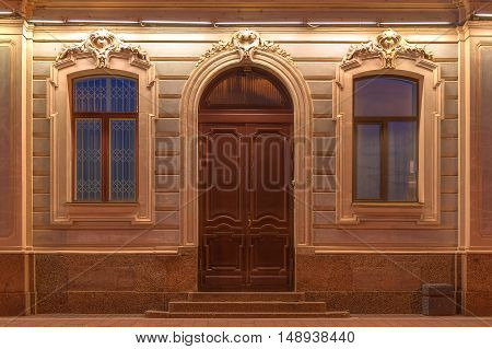 Two windows and door in a row on night illuminated facade of urban apartment building front view St. Petersburg Russia