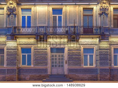 Several windows in a row balcony and door on night illuminated facade of urban apartment building front view St. Petersburg Russia