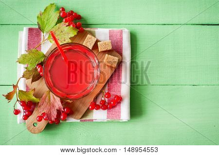 Fresh viburnum drink in glass on green wooden background with leaves and berries. Top view.